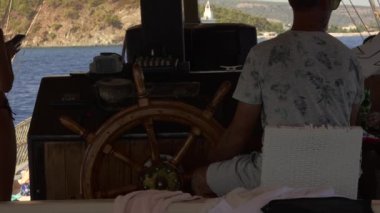 Bir denizci klasik bir ahşap tekerlek kullanarak bir tekneyi ustalıkla idare eder, sakin bir gökyüzünün altındaki manzaranın nefes kesici manzarasının tadını çıkarır..