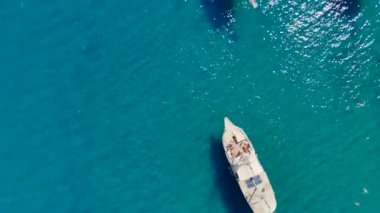 Yüzen turistlerle çevrili, berrak denizde demirlemiş beyaz turist yatlarının insansız hava aracı görüntüsü 360 derecelik bir perspektif sunuyor..