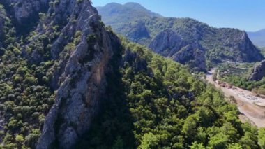 Turist ve yatların kıyı şeridinin keyfini çıkardığı, kristal berrak denizle karşılaşan Türk kayalık dağlarının çarpıcı insansız hava aracı görüntüsü. 