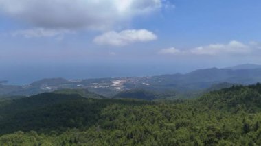 Bir dron dağlardaki sık ormanın panoramik görüntüsünü yakalar. Deniz ve yumuşak bulutlar çarpıcı bir zemin oluşturur..