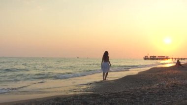 Genç bir kadın gün batımında sahilde koşuyor, gökyüzünün canlı renklerinin ve rahatlatıcı deniz esintisinin tadını çıkarıyor..