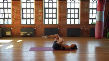 Spor giyimli genç bir kadın spor salonunda sırt bükme ve esneme egzersizi yapıyor. Yaralanmaları önlemek için omurilik hareketliliğini, esnekliğini ve kas gevşemesini geliştirmeye odaklanıyor..