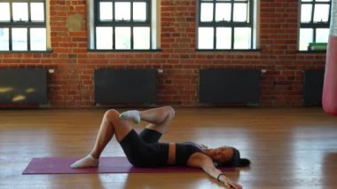 Spor kıyafetleri içinde formda genç bir kadın spor salonunda esneme egzersizleri yapıyor. Omurilik esnekliğini geliştirmeye, gerilimi azaltmaya ve genel duruşu geliştirmeye odaklanıyor..
