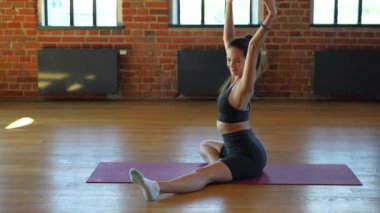 Spor giyimli formalı genç bir kadın spor salonunda ısınma egzersizi yapıyor. Yere uzanır, esnekliğini, duruşunu ve kas gücünü arttırır..