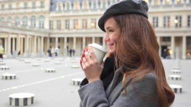 Paris 'teki Royal Palace Meydanı' nda elinde bir fincan kahveyle gülümseyen bir kız duruyor. Mutluluk saçıyor. İkonik bir Fransız ortamında şık kıyafetler giyiyor..