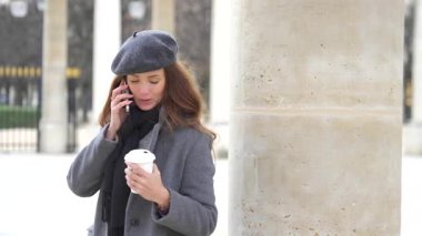 Paris 'te elinde bir fincan kahve olan bir kız, Place Royal Palace' ın tarihi sütunlarının yanında telefonla konuşuyor. Kamera hareketi dinamik ve modern bir dokunuş ekler..