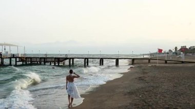 Bir kadın kumsalda yürürken nefes kesici bir gün batımı ufku aydınlatır. Dalgalar rahatlatıcı bir atmosfer yaratırken ayak izleri kumlarda kaybolur..