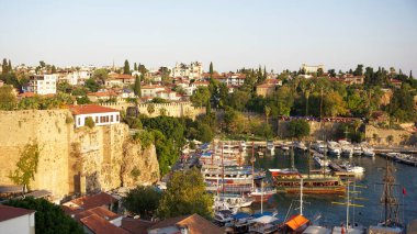 Türkiye, Antalya - 29 Eylül 2024: Rıhtım boyunca kayıkları olan canlı bir liman, yemyeşil ve taştan tahkimatları olan tarihi bir kasabaya karşı kuruldu