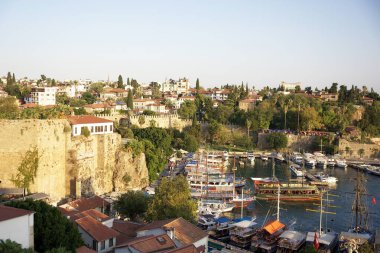 Türkiye, Antalya - 29 Eylül 2024: Yeşillik, antik tahkimatlar ve tekne ve yatlarla dolu bir marina ile tarihi bir kıyı kasabasının manzarası.