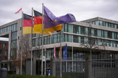 Berlin, Almanya 02.13.2025 Çok sayıda Alman ve Avrupa Birliği bayrakları Berlin 'deki modern bir ofis binasının önünde rüzgarda dalgalanmakta, hükümet veya kurumsal varlığı temsil etmektedir..