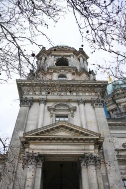 Yapraksız dallarla çerçevelenmiş Berlin Katedrali 'nin yukarıdan görünüşü bulutlu gökyüzüne karşı büyük barok mimarisini sergiliyor..