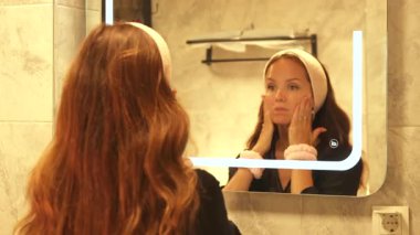 Banyo masajında genç ve güzel bir kadın aynanın önünde yüzünü yıkayıp cildini serinletiyor.. 