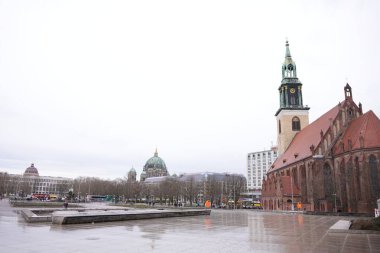 Berlin, Almanya 02.13.2025 Islak bir şehir meydanında kubbeli bir katedrali, modern binaları ve arka planında yayaları olan tarihi tuğla bir kilise bulunuyor..