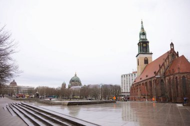 Berlin, Almanya 02.13.2025 Islak bir şehir meydanında kubbeli bir katedrali, modern binaları ve arka planında yayaları olan tarihi tuğla bir kilise bulunuyor..