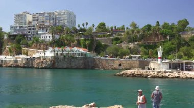 Türkiye, Antalya 10 Ekim 2024 Deniz feneri, botlar ve yemyeşil yemyeşil manzaralı bir sahile sahip iki erkek marinanın kayalık sahillerinde balık tutuyor.. 