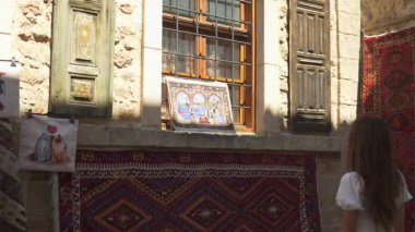 Türkiye, Antalya 10 Ekim 2024 'te akıcı beyaz elbiseli bir kadın, renkli el yapımı halı ve tekstil ürünleriyle çevrili bir pencerede örülmüş dekoratif bir sanat eserini gözlemledi..