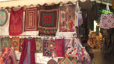 Türkiye, Antalya 10 Ekim 2024. Bir pazarda geleneksel el yapımı halılar, dokuma kumaşlar ve dekoratif çantalar sergileniyor. Karmaşık desenler ve kültür işçiliği vurgulanıyor.