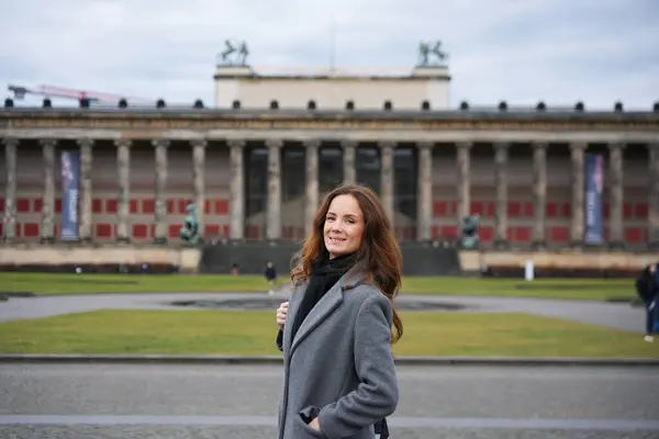 Gri ceketli, gülümseyen bir kadın, arka planda neoklasik sütunlarıyla Almanya 'nın Berlin kentindeki tarihi Altes Müzesi' nin önünde bir anın tadını çıkarıyor.. 