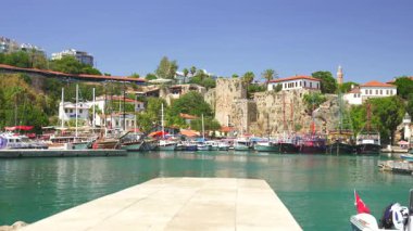 Türkiye, Antalya 10 Ekim 2024 tarihi bir liman manzarası, renkli tekneler, antik taş tahkimatları ve açık mavi gökyüzünün altında yemyeşil bir yer.. 