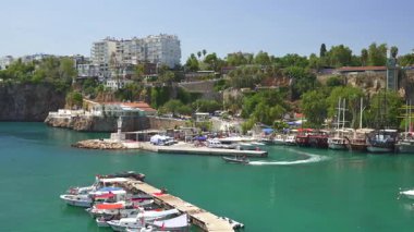 Türkiye, Antalya 10 Ekim 2024 Turkuaz suları boyunca kenetlenmiş, engebeli kayalıklar ve arka planda modern binaların yer aldığı bir şehir manzarası olan pitoresk bir sahil limanı.