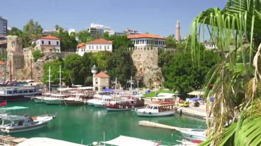 Türkiye, Antalya 10 Ekim 2024 tarihi taş binalar ve yemyeşil yeşilliklerle çevrili çarpıcı turkuaz sular boyunca yanaşmış yatları ve ahşap tekneleri olan pitoresk bir Akdeniz limanı.