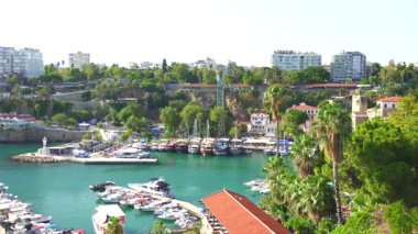 Türkiye, Antalya 10 Ekim 2024 Limanı, turkuvaz suları boyunca kenetlenmiş yatlar ve yelkenliler, yemyeşil, tarihi mimari ve arka planda modern bir şehir manzarası ile çevrili.. 