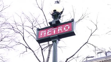 Bir sokak lambasına asılmış klasik bir Paris metrosu tabelası. Etrafı çıplak kış ağaçlarıyla çevrili. Sonsuz Paris cazibesi ve zarafeti sergiliyor.. 