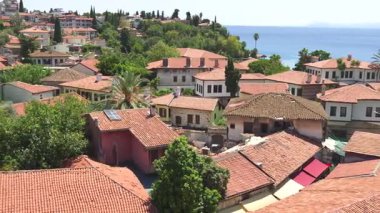 Osmanlı tarzı kırmızı çatı evleri, yemyeşil ağaçlar ve tarihi taş mimarinin yer aldığı Antalya 'nın eski kentinin manzaralı fotoğrafı. 