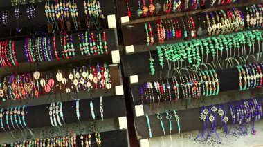 Bir pazar yerinde sergilenen renkli değerli taşlar, deniz kabukları ve tılsımlardan oluşan el yapımı kolye koleksiyonu, zanaatkarlık ve kültürel tasarımı ön plana çıkarıyor..