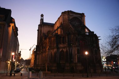 Brüksel Belçika 03.25.2025 Alacakaranlıkta parlayan sokak lambaları ve sakin bir şehir sokağının tarihi Avrupa 'ya sıcaklık kattığı bir kaldırım taşı meydanının üzerinde dramatik bir Gotik katedral beliriyor..