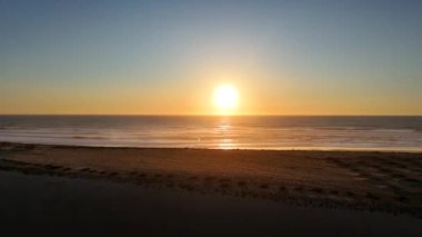 Kum tepeleri olan ıssız bir kumsalın havadan görüntüsü, sakin sahil şeridi boyunca altın günbatımı ışığı sırasında drone tarafından yakalandı..