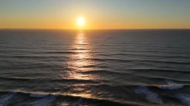 Okyanus ufkunun üzerinde altın güneş batıyor, sakin ve manzaralı deniz manzaralı yumuşak dalgalara sıcak yansımalar yapıyor.. 