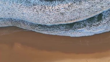 Okyanus dalgalarının havadan görünüşü sakin kıyı şeridi boyunca uçan bir dron gibi altın kumla ıssız bir sahili nazikçe yıkıyor.. 