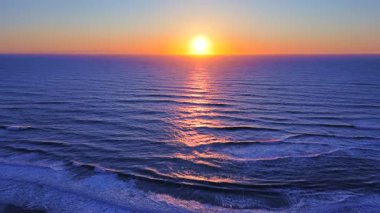 Sakin okyanus üzerinde altın gün batımı, yumuşak dalgalar ve parıldayan ışıkla birlikte sakin doğa ve seyahat görselleri için ideal bir atmosferik deniz manzarası yaratıyor.. 