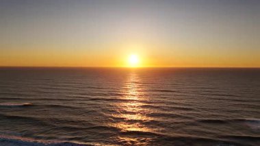 Sakin okyanus üzerinde altın gün batımı, yumuşak dalgalar ve parıldayan ışıkla birlikte sakin doğa ve seyahat görselleri için ideal bir atmosferik deniz manzarası yaratıyor.. 
