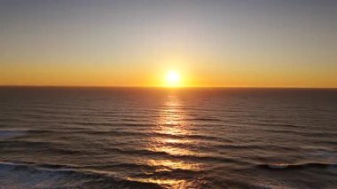Altın gün batımında sakin okyanusun üzerinde uçan drone, yumuşak dalgalar üzerinde parıldayan güneş ışığını yakalıyor ve sakin bir deniz manzarasında doğa, seyahat veya arka plan görselleri için mükemmel.. 