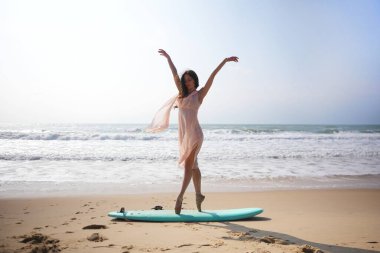 Dalgalar hafifçe çarpar ve mükemmel bir şekilde dengede durur. Harekete geçmiş bir dansçı, pembe elbisesi esintiye kapılmış dinginliğe tutunuyor.. 