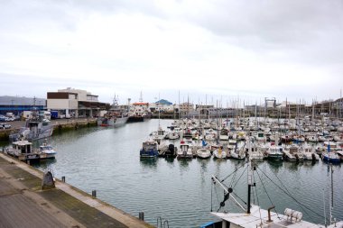 Boulogne. Fransa 03.28.2025 Balıkçı tekneleri ve sanayi kıyısı binaları ve bulutlu gökyüzünün altında devriye gemileri ile dolu büyük bir marina.. 
