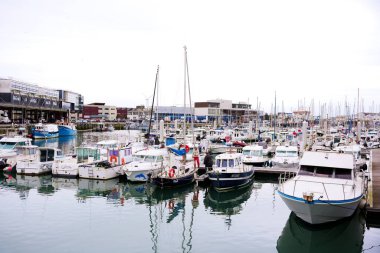 Boulogne. Fransa 03.28.2025 Şehir Marinası sanayi binaları yakınında çeşitli küçük tekne ve yatlarla dolu bulutlu gökyüzü altında sakin suya yansıyor.. 