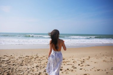 Yazlık elbiseli bir kadın kokteylini sanki denize kadeh kaldırır gibi kaldırır. Neşenin, güneşin ve kaygısız sahil kutlamalarının sembolü.. 