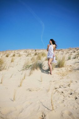 Beyaz, dalgalı bir yaz elbisesi içinde genç bir kadın güneşli kum tepeciklerinde yalınayak yürüyor, canlı mavi gökyüzünün altında kuru çimlerle çevrili, özgürlük, huzur ve gezgin şehvet hissini yakalıyor.. 