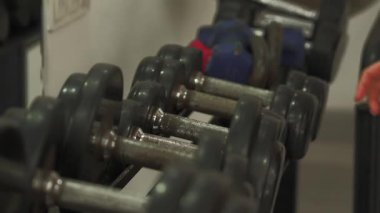 Kadın elleri, raftan bir dambıl almaya uzanırken, modern spor salonunda güç antrenmanına hazırlanıyor.. 