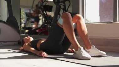 Doğal ışıklandırılmış spor salonunda yoga minderindeki kalça aktifleştirmesi için direnç bandı kullanan düşük vücut kuvveti egzersizi..