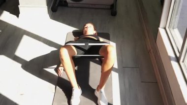 Yoga minderinde bantlı kalça köprüsünü güçlendirmek, doğal ışık spor salonunda vücut kaslarını geliştirmek..