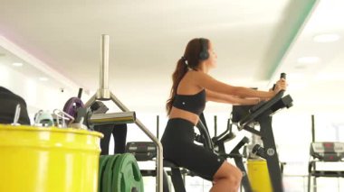 Sabit bisiklete odaklanmış kardiyo seansı, spor giyim ve kulaklık takan kadın modern spor salonunda yoğun pedallar.. 