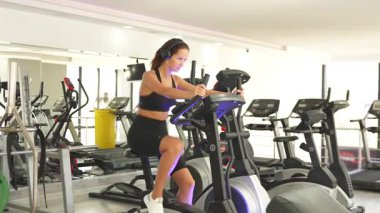 Modern bir spor salonunda eliptik kulaklık takan kadınlar doğal ışıkla dolu, kardiyo, hareket ve sağlığa odaklanıyor.. 