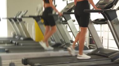 Siyah spor giyim giymiş atletik bir kadın koşu bandında koşar, aynada yansıması görünür, kardiyo çabasını ve vücut çalışmasını ön plana çıkarır.. 