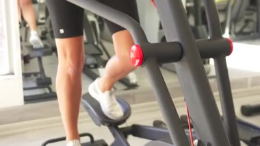 Spor salonundaki atletik kadın, eliptik antrenör kullanıyor, orta adım, kulaklık takıyor ve odaklanmış, kararlı bir egzersiz duruşu sergiliyor.. 