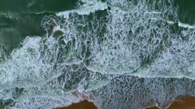 Geniş açılı insansız hava aracı çekimi, yumuşak dalgalar, beyaz köpük ve uzaklığa uzanan parlak mavi gökyüzü ile huzurlu bir okyanus manzarası gösteriyor..