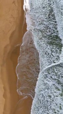 Hava aracı, köpüklü dalgaları, detaylı dokuları ve sisli bir gökyüzünün altındaki lastik izlerini gösteren kumlu bir sahili görüntülemek için yer değiştiriyor..